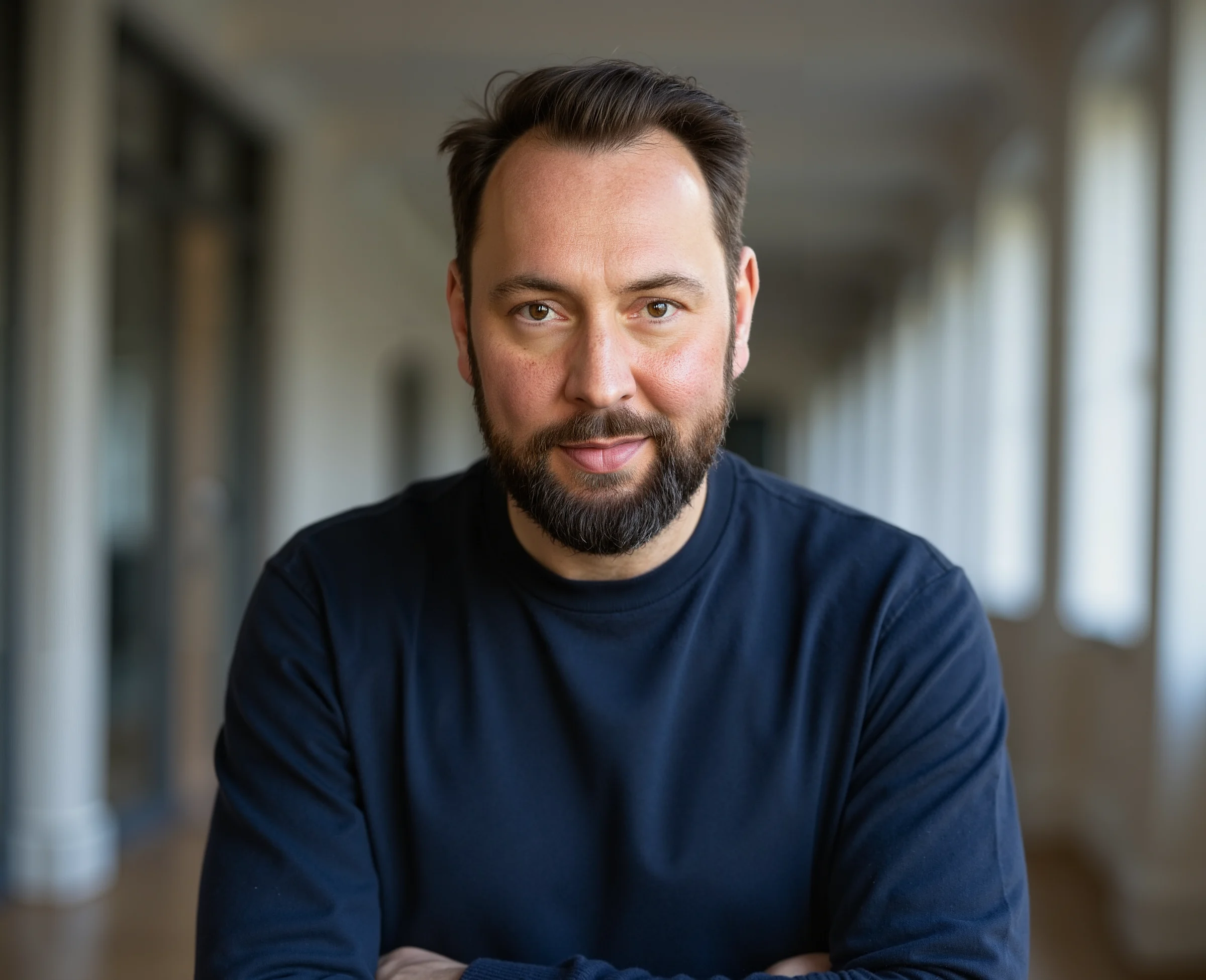 Portrait of Adam Birley in a navy top, with a corridor behind him